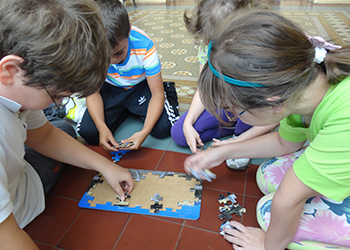 Um grupo de crianças montando um quebra-cabeças. O jogo está no chão, no centro da foto.