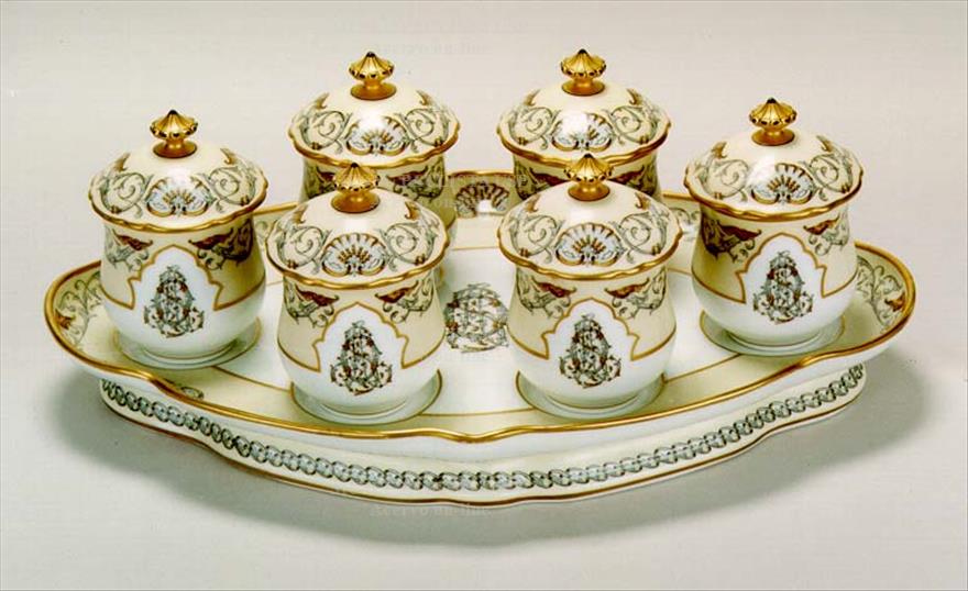Set of crockery, with a large oval-shaped plate on which there are 6 small pots with lids.