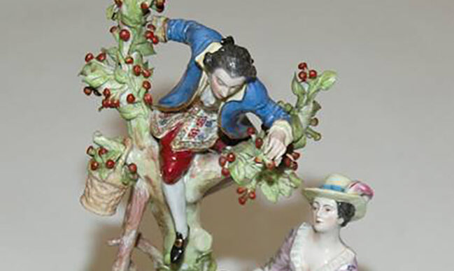 Small porcelain sculpture representing a man and a woman. The man is on top of a tree picking fruit.