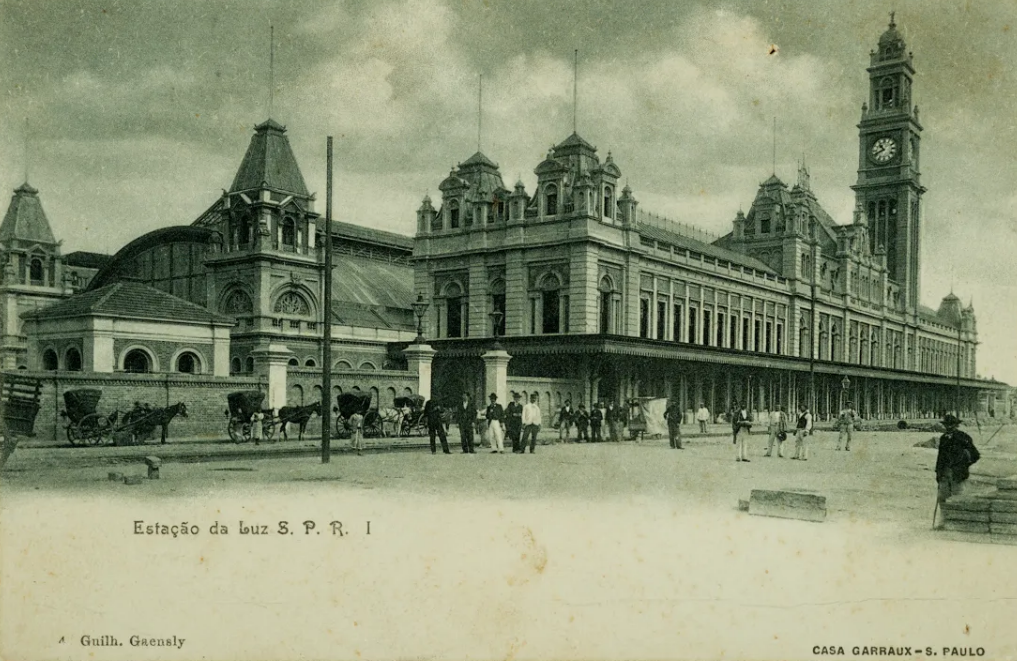 Fotografia da Estação da Luz feita em 1904. À frente da estação são vistas pessoas, charretes e cavalos.