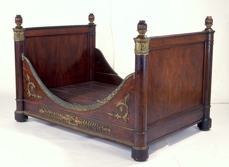 Uma cama de madeira, com dois lados com grandes tábuas quadradas. Nos outros, duas madeiras baixas em formato côncavo.