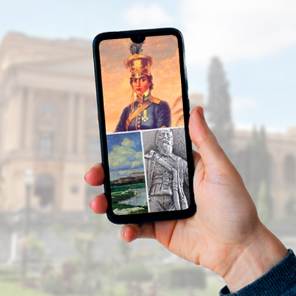 A hand holding a cell phone. On the screen, images of works from the collection of the Ipiranga Museum.