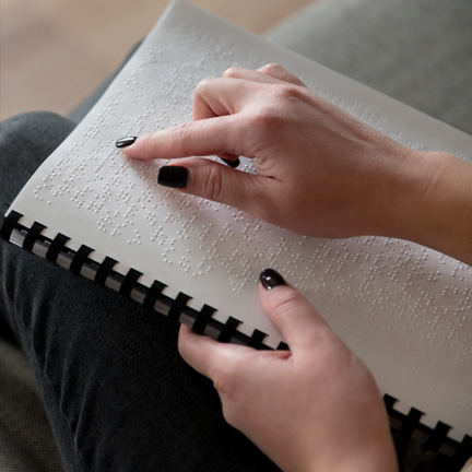 Mãos de uma pessoa manipulando um caderno com texto em braille.
