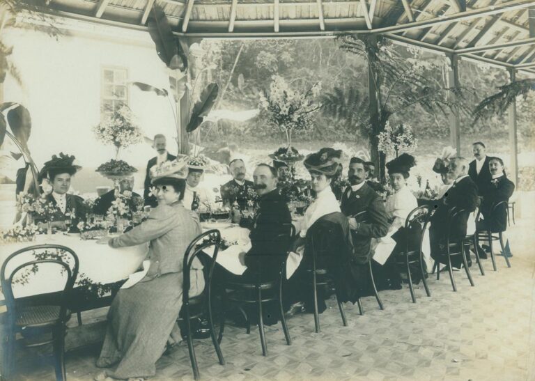Fotografia histórica em preto e branco mostra homens e mulheres em banquete formal, com mesa decorada e arranjos florais, relacionada ao Encontro com a Pesquisa – março de 2026, no Museu do Ipiranga.