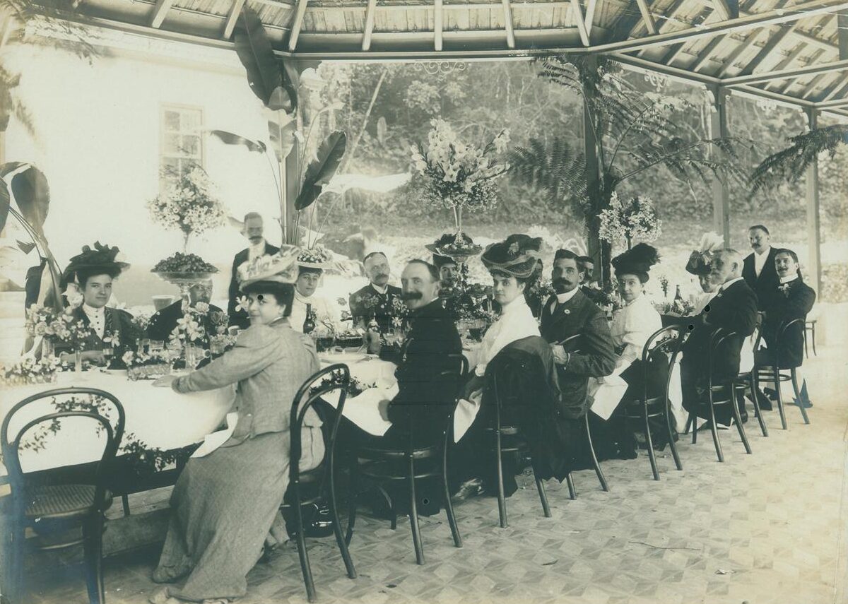 Fotografia histórica em preto e branco mostra homens e mulheres em banquete formal, com mesa decorada e arranjos florais, relacionada ao Encontro com a Pesquisa – março de 2026, no Museu do Ipiranga.