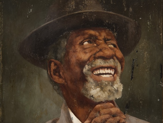 homem negro sorridente com as mãos cruzadas usa chapéu